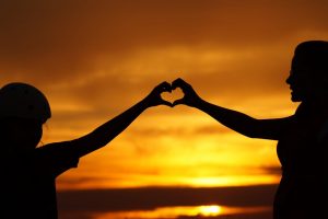 Two People creating a heart with their hands in front of a sunset