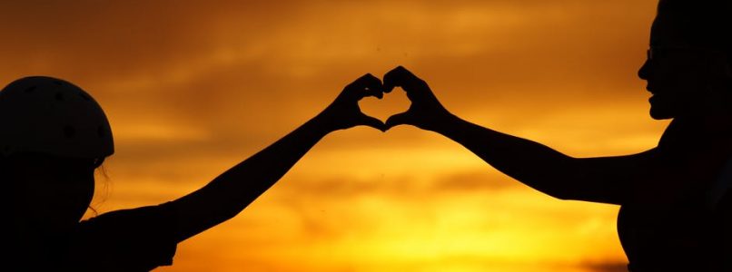 Two People creating a heart with their hands in front of a sunset