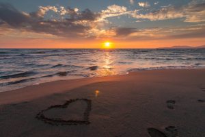 Sunset from a beach with a heart drawn in the sand