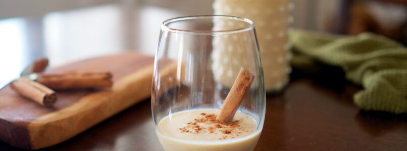 Egg nog and cinnamon stick in a glass.